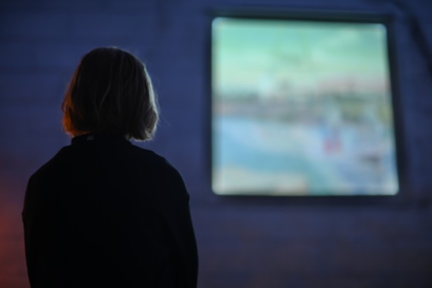 Une jeune fille de dos regarde retroprojection vidéo présentée dans une fenêtre de l'édifice de La Filature.